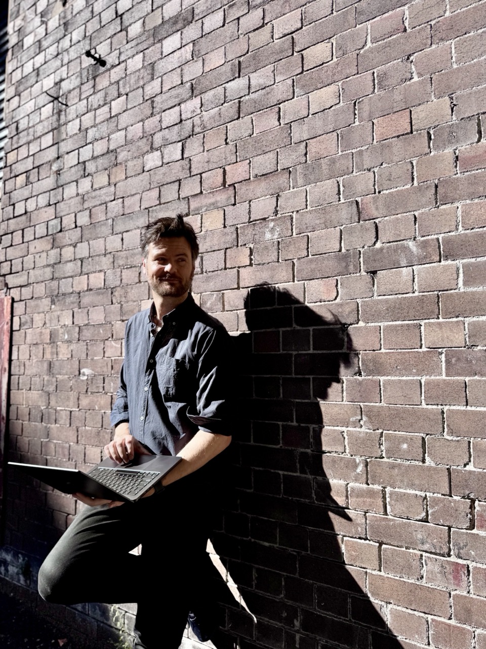 Stafford from Pirrama Tech, leaning against a brick wall with a laptop